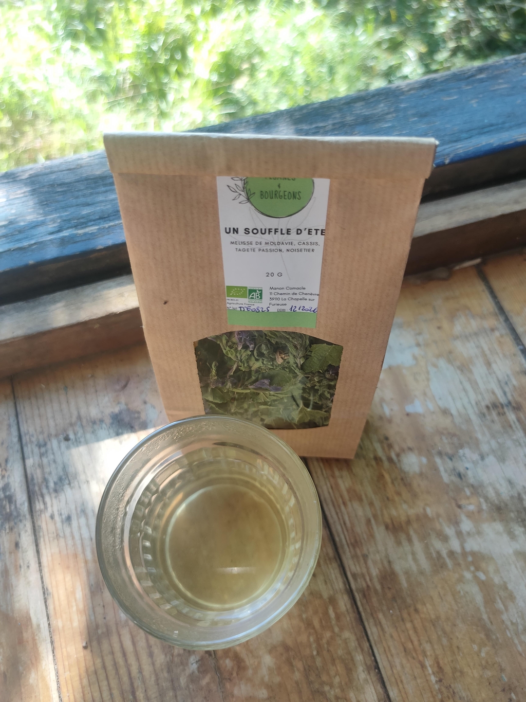 Sachet de tisane "Un souffle d'été", un mélange de Tisanes et Bourgeons, avec un verre de tisane devant.