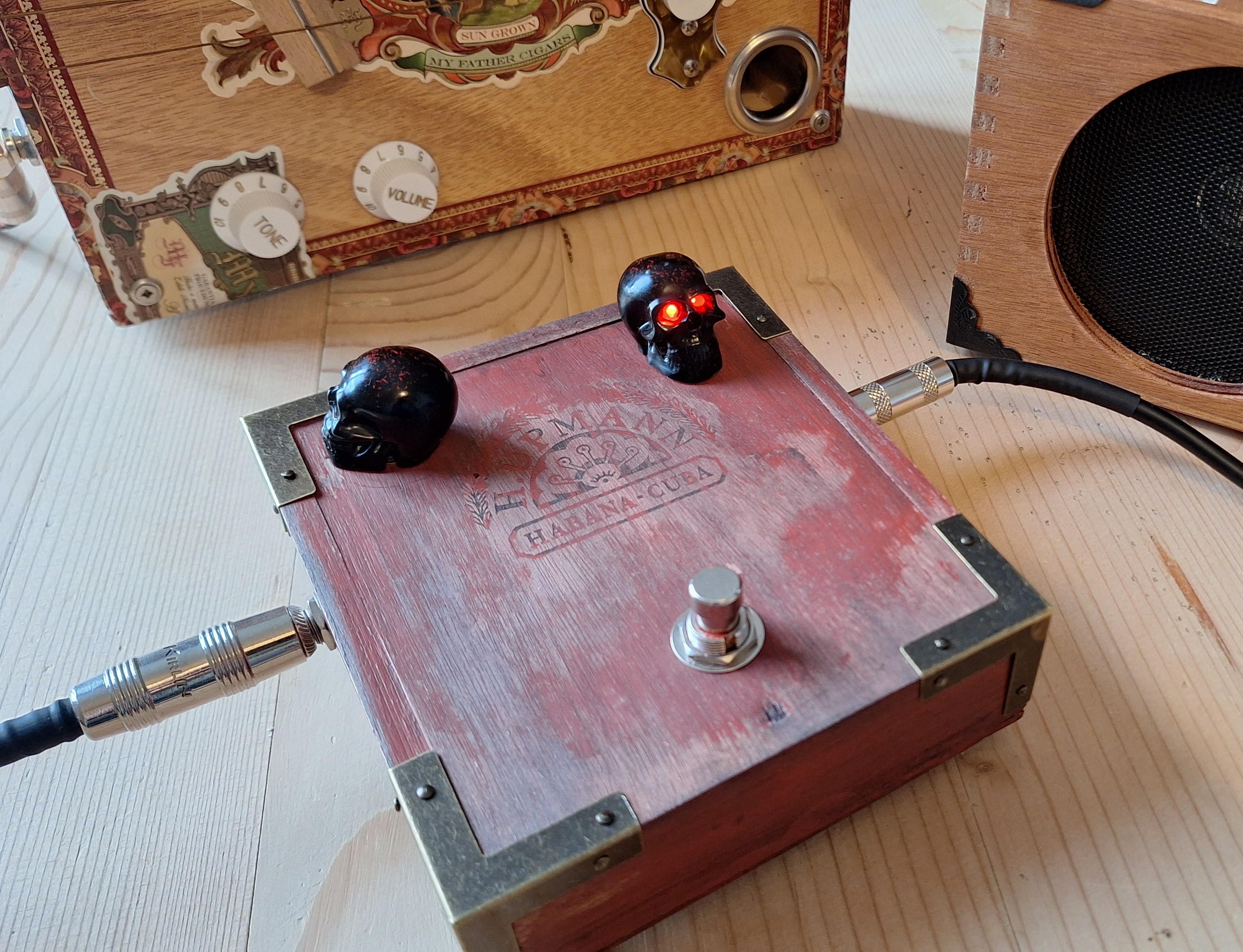 Guitar Effects Pedals section with a photo of a cigar box containing an effects pedal with black skull knobs. One of the skulls has red LEDs for eyes.
BoxAmps make portable guitar amps and speakers for music playback. Hancrafted in France