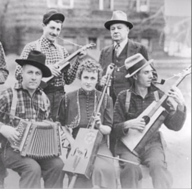 Black and white photo of  a group of musicians with rudimentary musical instruments. 