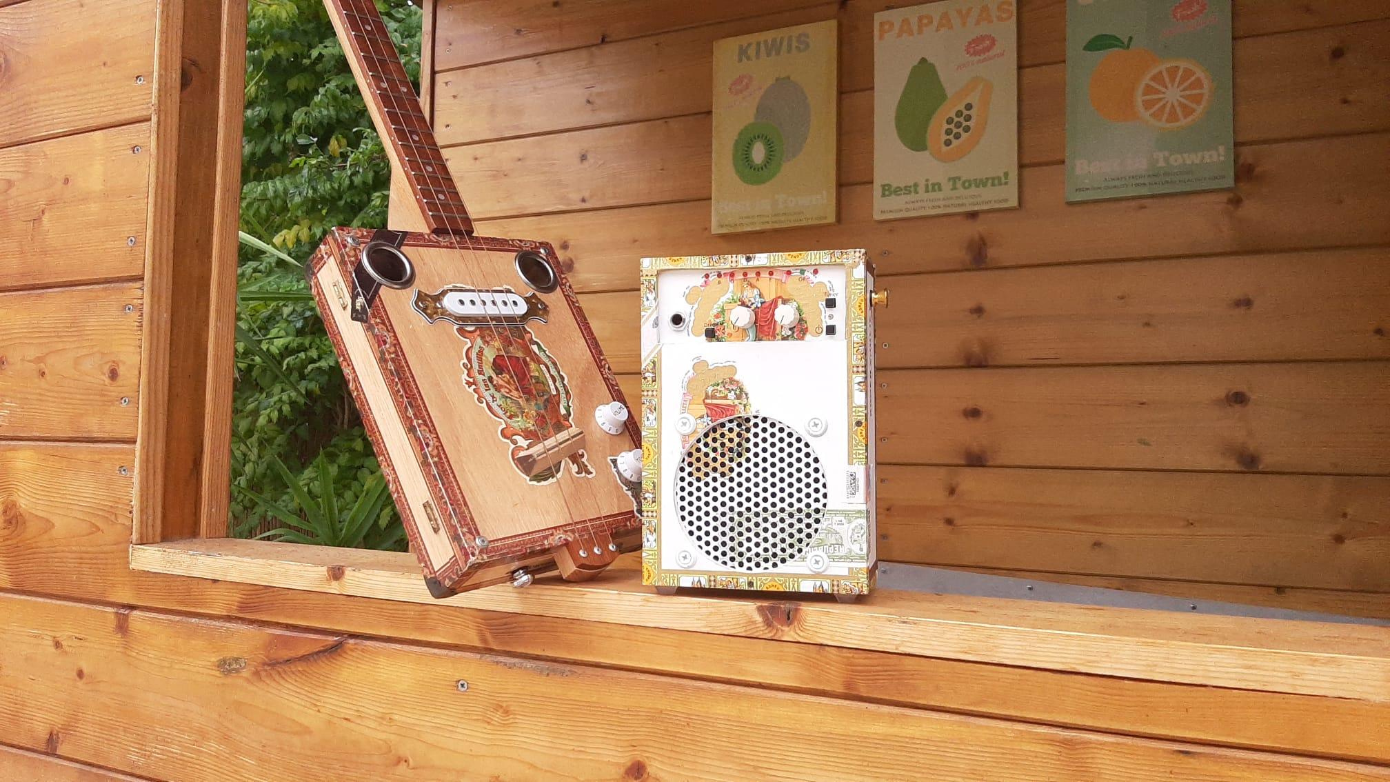 A handcrafted Romeo y Julietta cigar box amplifier made in France on the Presquîle de Giens. It is photographed next to a cigar box guitar (CBG). BoxAmps make portable guitar amps and speakers for music playback. Custom made in France
