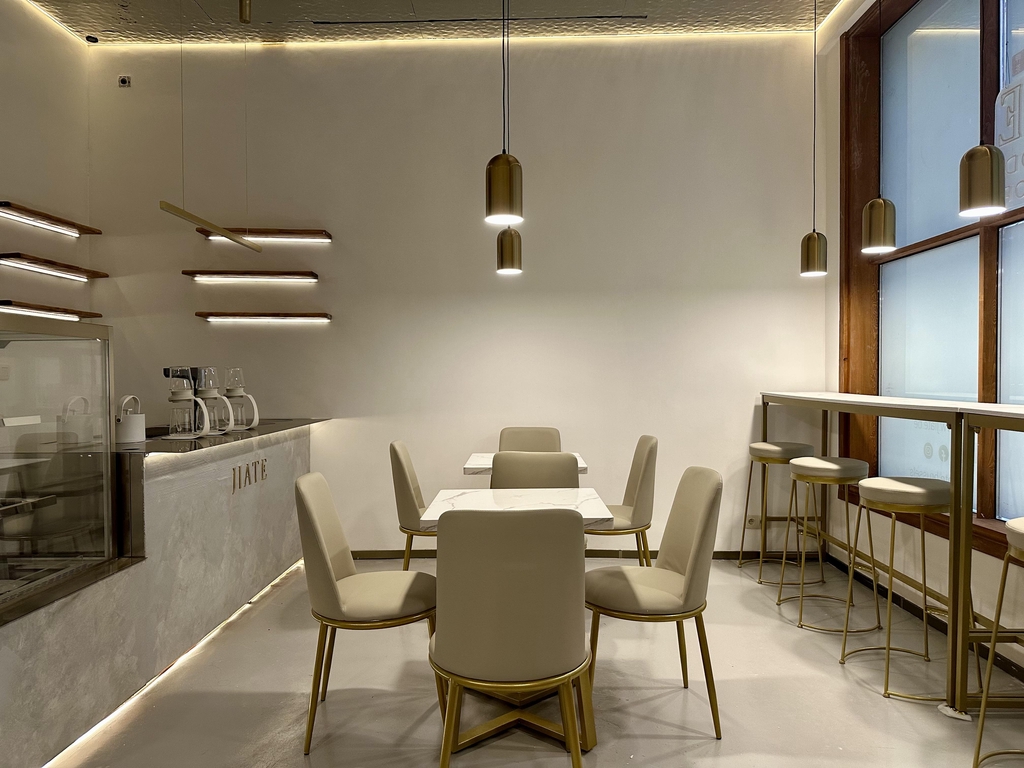 Minimalist interior of JIATÉ teahouse in Brussels with marble tables, gold-accented chairs, and warm pendant lighting in a cozy modern setting.
