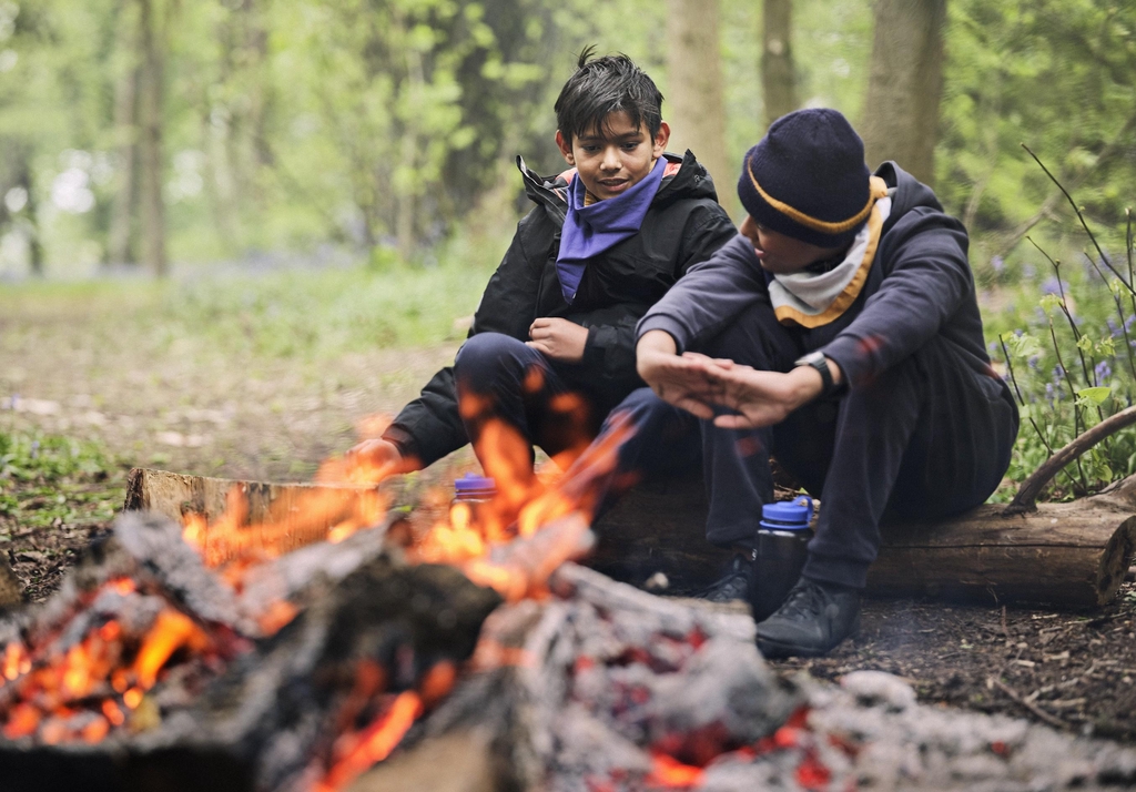 Scouts outside by a camp fire chatting, belonging.