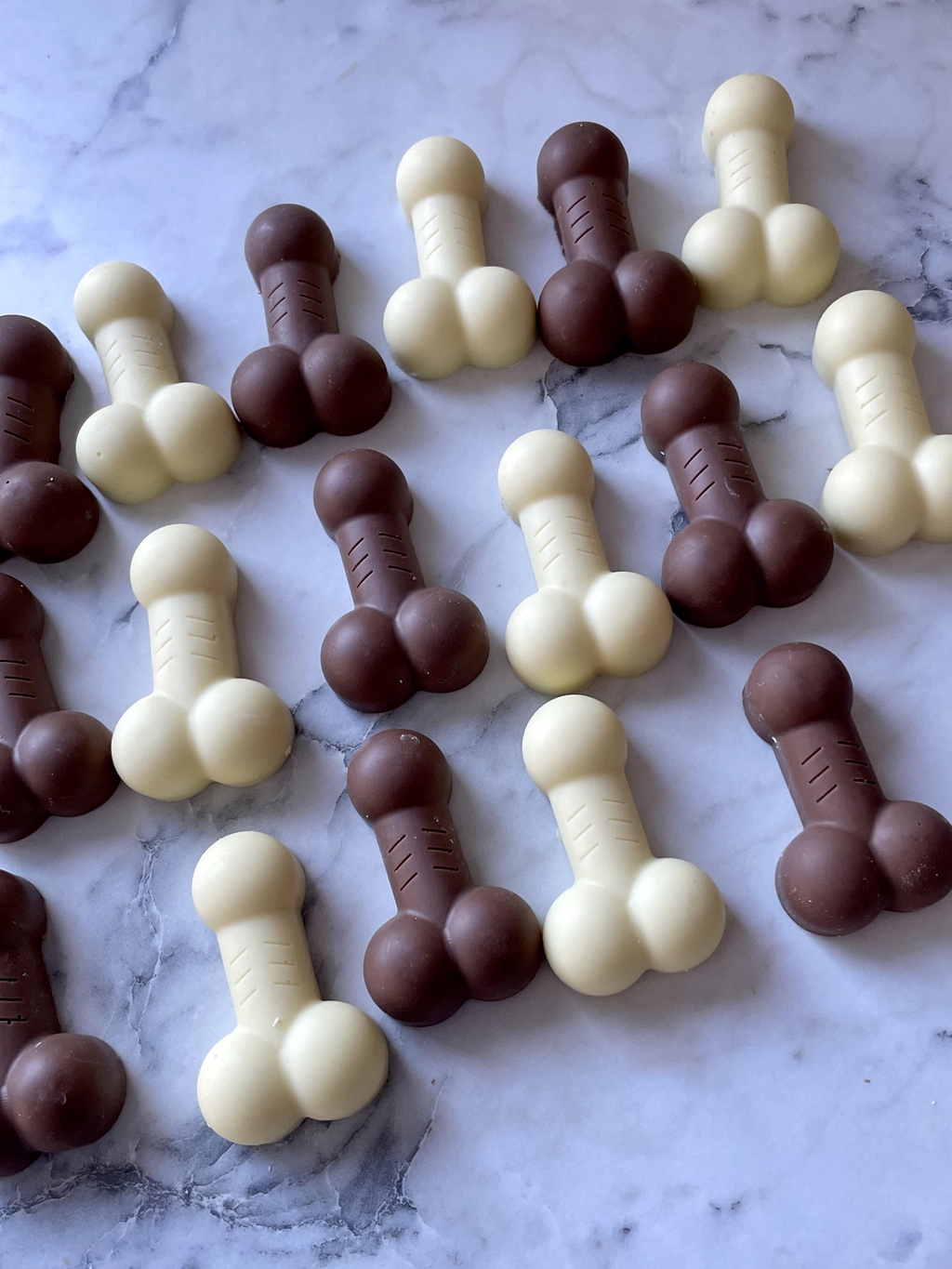 Cheeky handmade chocolate willy treats in milk and white chocolate, laid out on a marble background
