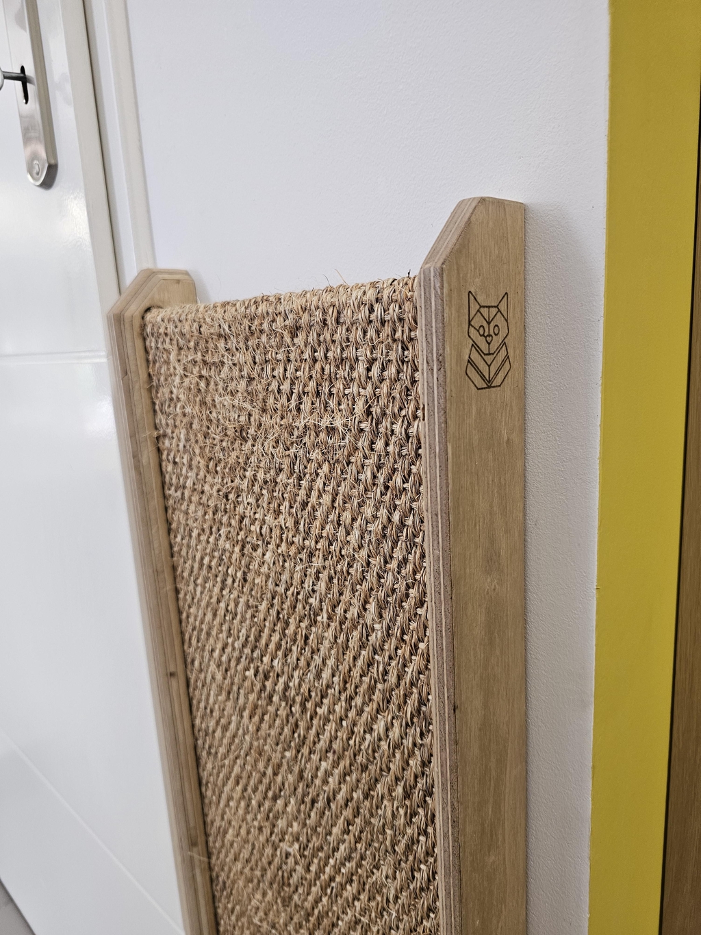Griffoir mural pour chat en bois de peuplier artisanal et sisal naturel tressé, installé à côté d'une porte blanche dans un intérieur moderne, signé Chat Envoie du Bois.