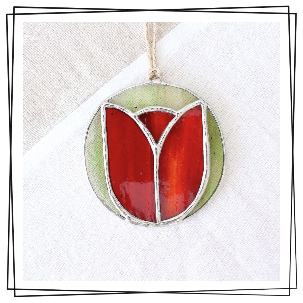Photo de Atelier Vitraï montrant une suspension en vitrail représentant une tulipe rouge sur un fond vert.