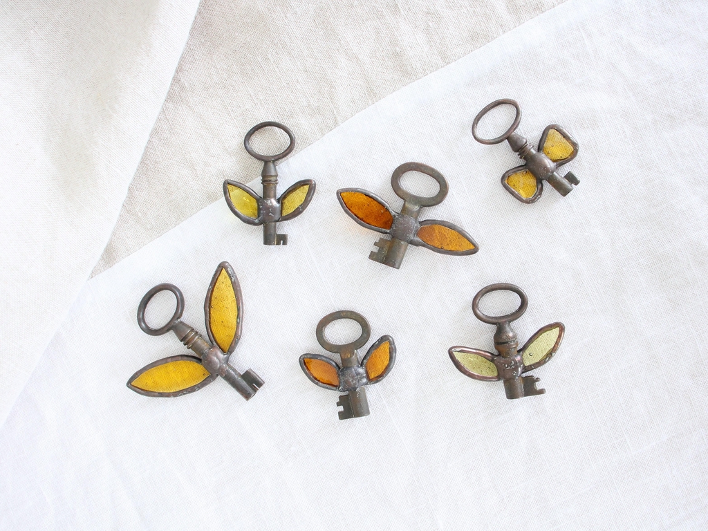 Photo de Atelier Vitraï montrant plusieurs petites clés ornées d'ailes en verre jaune et orange.
