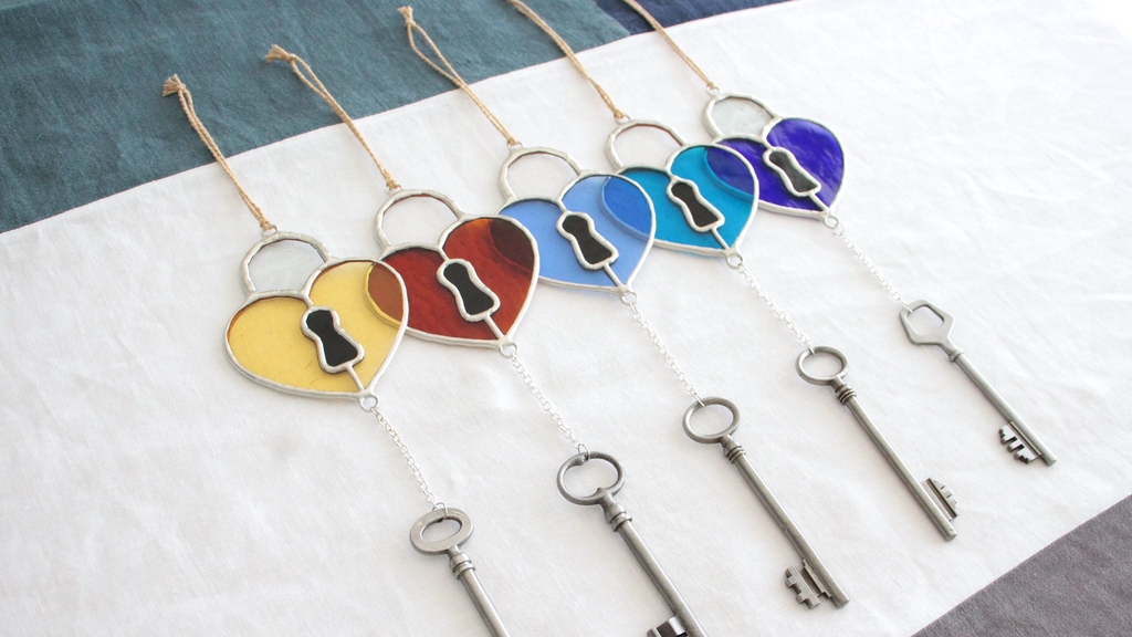 Photo de Atelier Vitraï montrant cinq suspensions colorées en vitrail en forme de cœur, chacune étant accompagnée d'une grande clé en métal argenté accrochée au bout d'une chaîne.