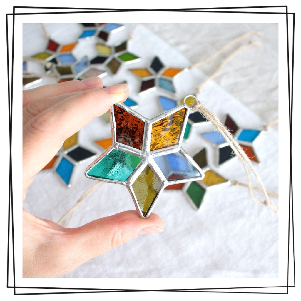 Photo de Atelier Vitraï montrant une étoile à cinq branches en vitrail multicolore, tenue par une main.