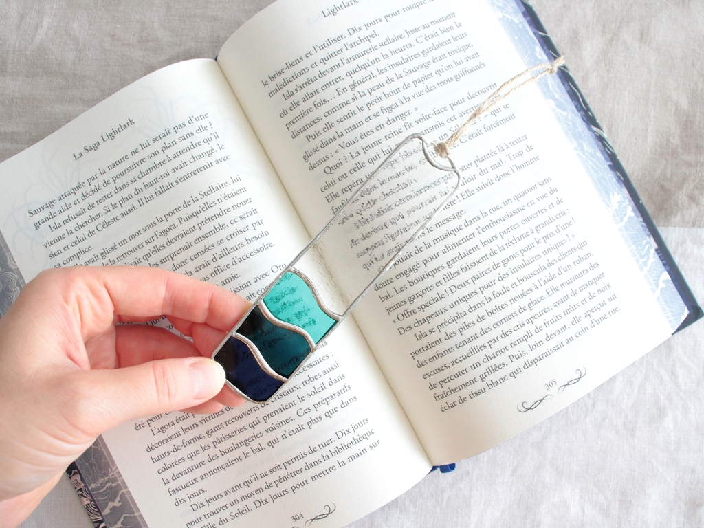 Photo de Atelier Vitraï montrant un marque-page en vitrail tenu par une main au-dessus d'un livre ouvert.