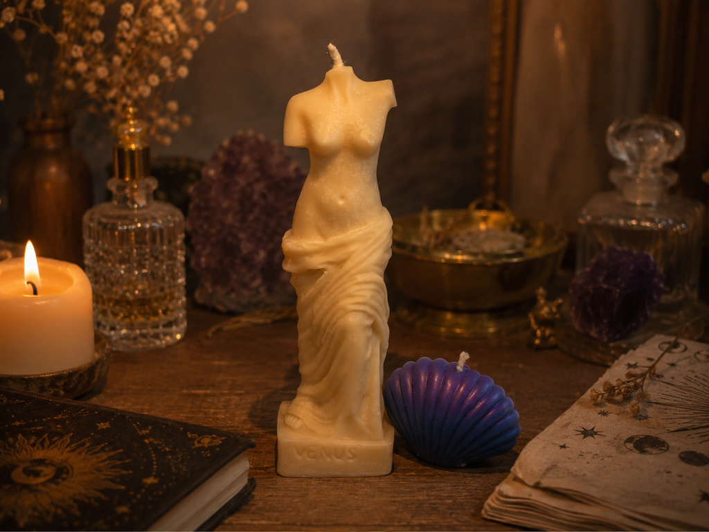 Bougie sculptée blanche représentant Aphrodite, entourée de bougies, de cristaux et d’objets décoratifs dans une ambiance chaleureuse et tamisée.
