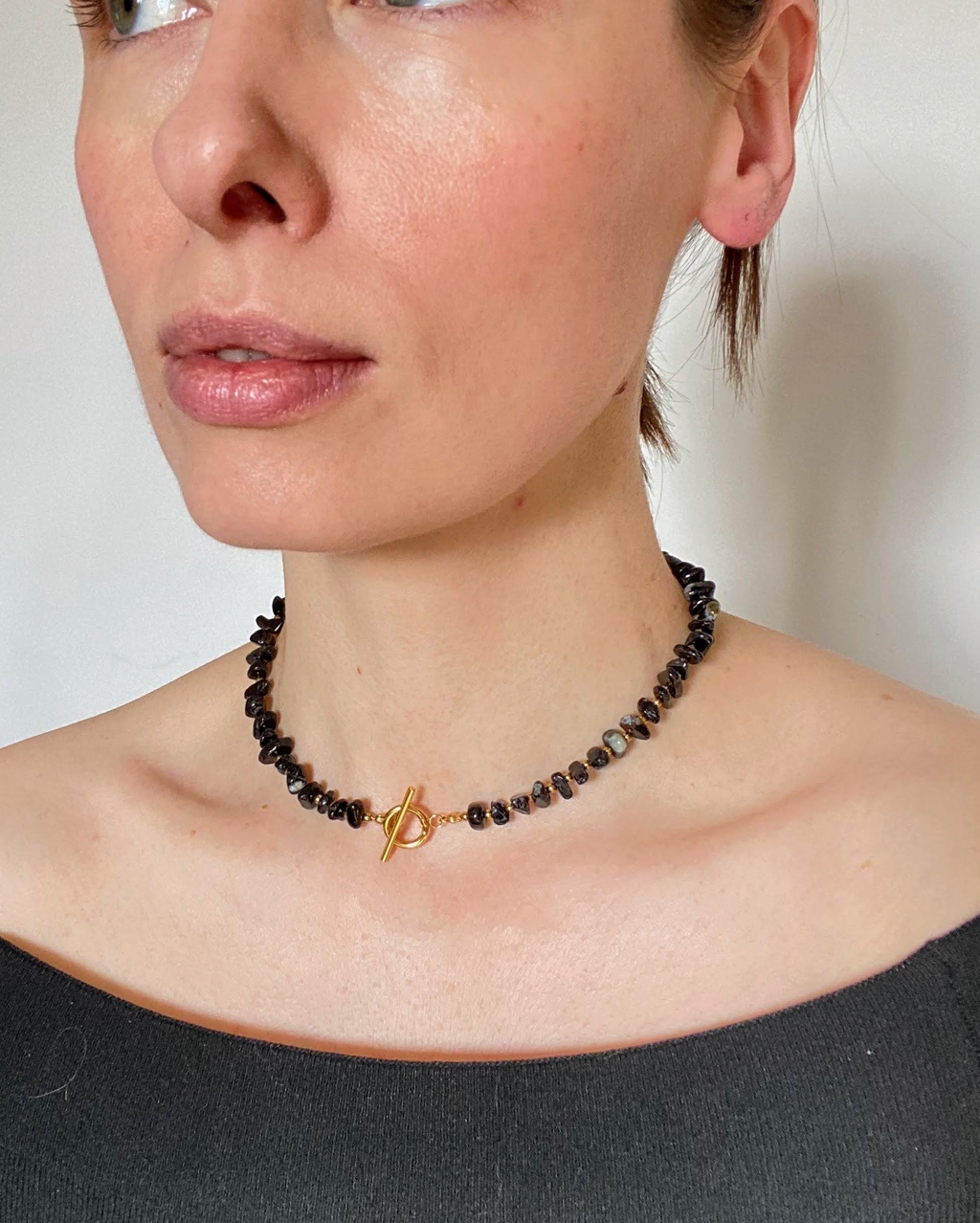 Bracelet et boucles d’oreilles assortis en acier inoxydable doré avec éclats d’agate noire, portés au poignet et aux oreilles. 