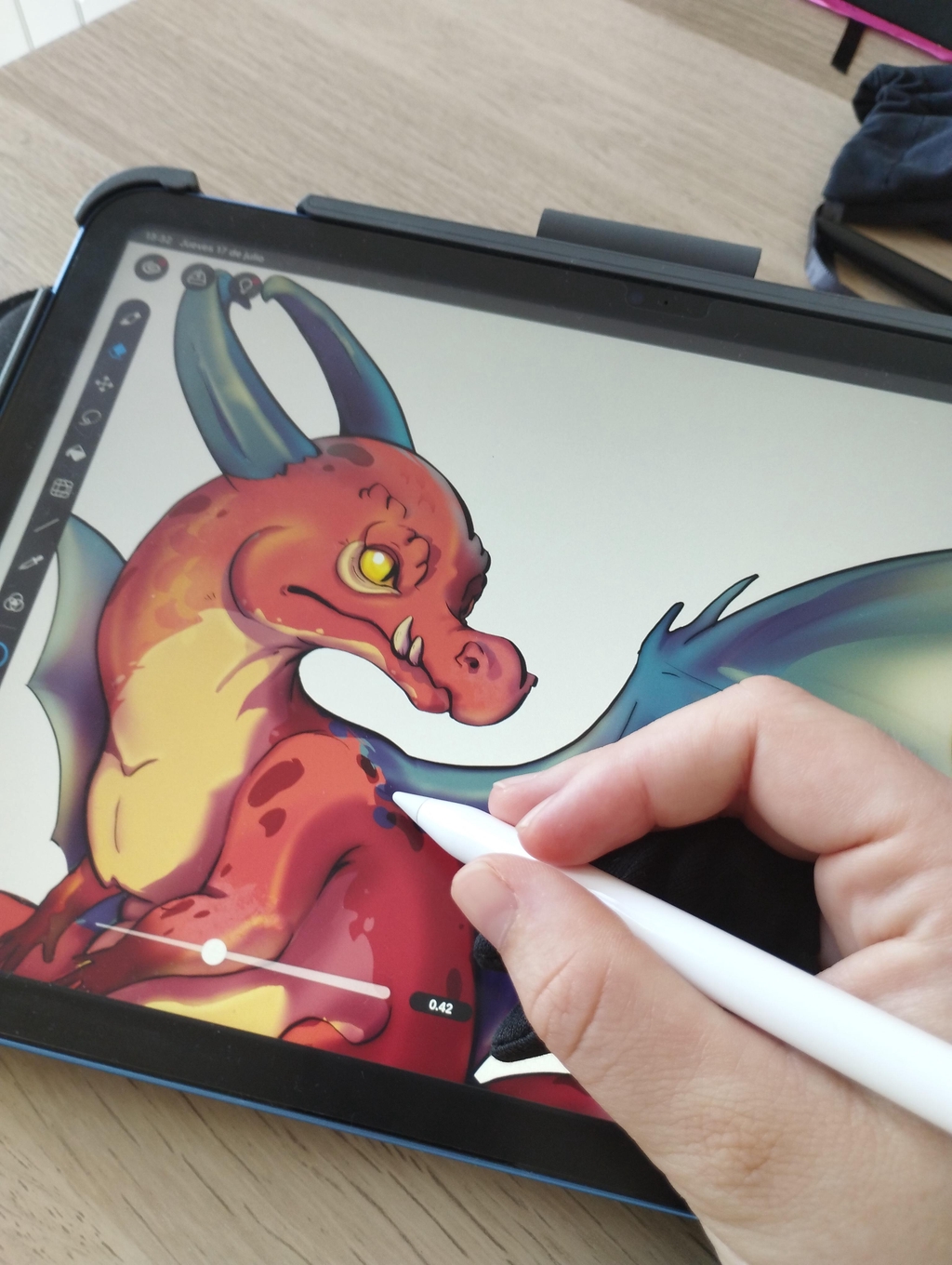 Dibujando un dragón rojo en el ipad, se ve una pantalla y una mano con un lápiz blanco dibujando en ella. 
