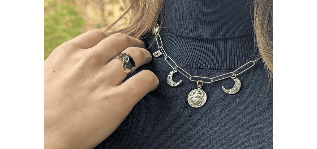 Collier chaîne argenté avec breloques lune, scarabée et œil, porté avec une bague chevalière — bijoux fantaisie Les Althëis inspirés de la mythologie.