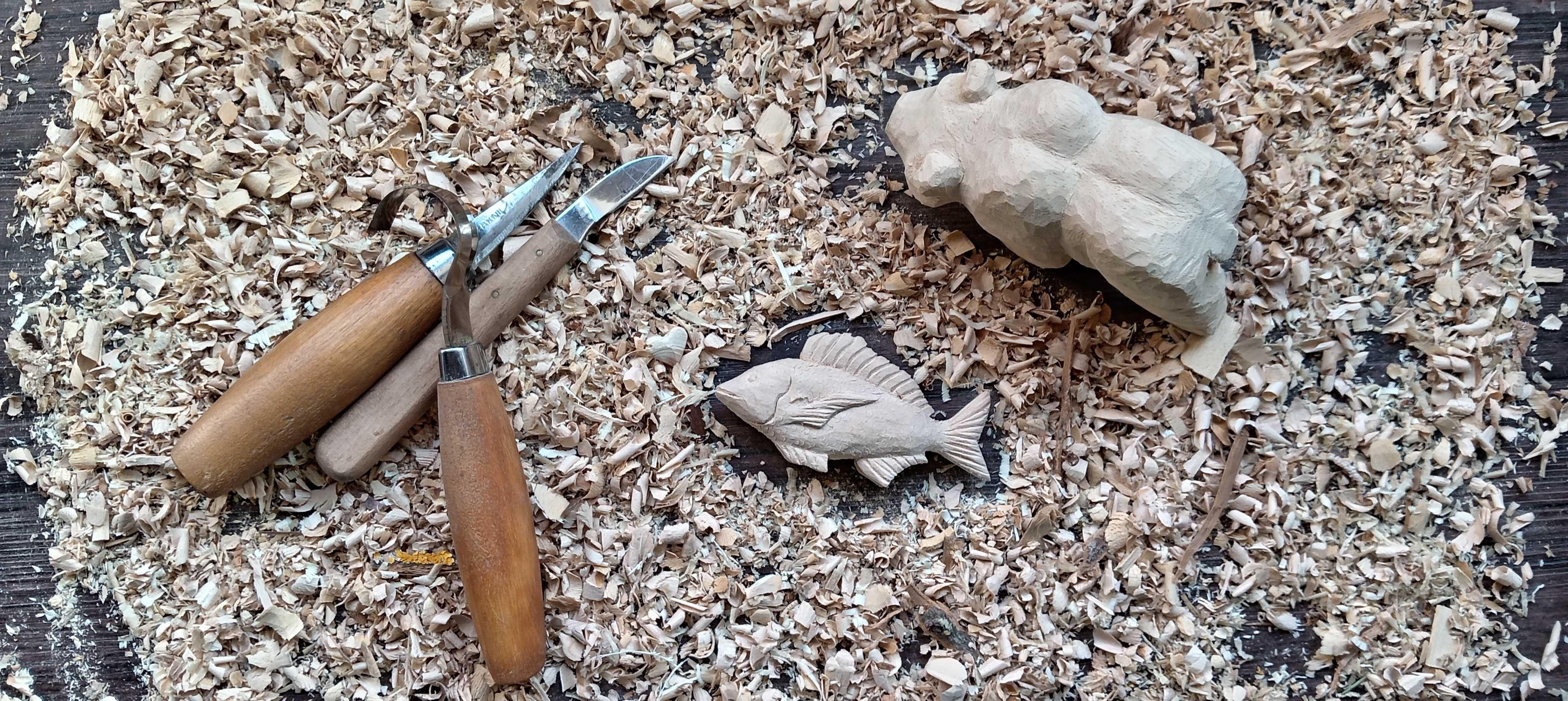 Ours et poissons sculptés dans du bois de tilleul posés sur un lit de copeau de bois avec des outils de sculpture. 