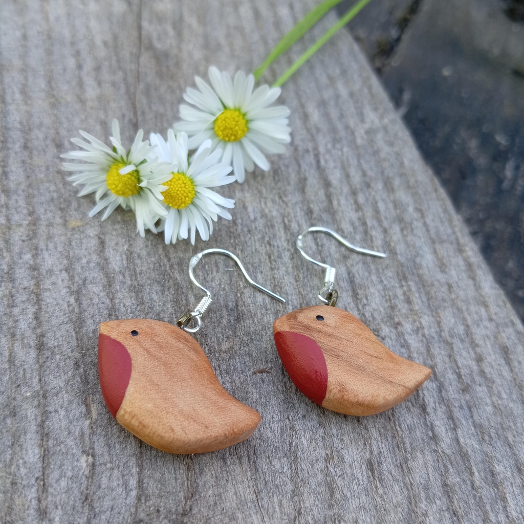 Paire de boucles d'oreilles en bois avec attaches en argent en forme de petits oiseaux sur du bois grisé avec trois pâquerettes.