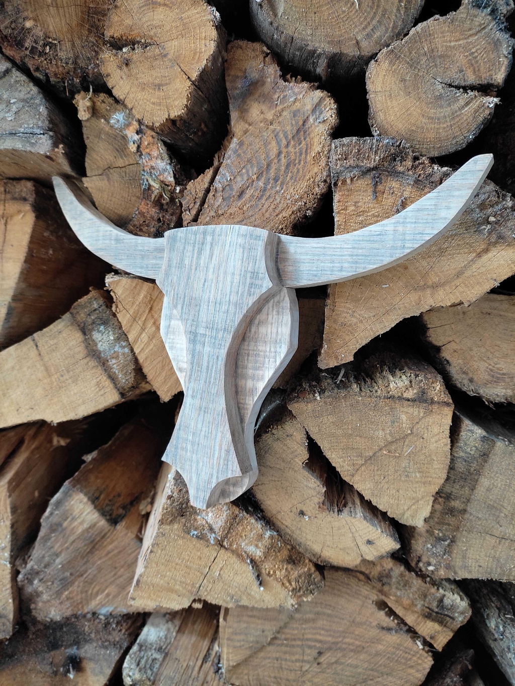 Tête de vache en bois de palette grisée accrochée sur du bois de chauffage.