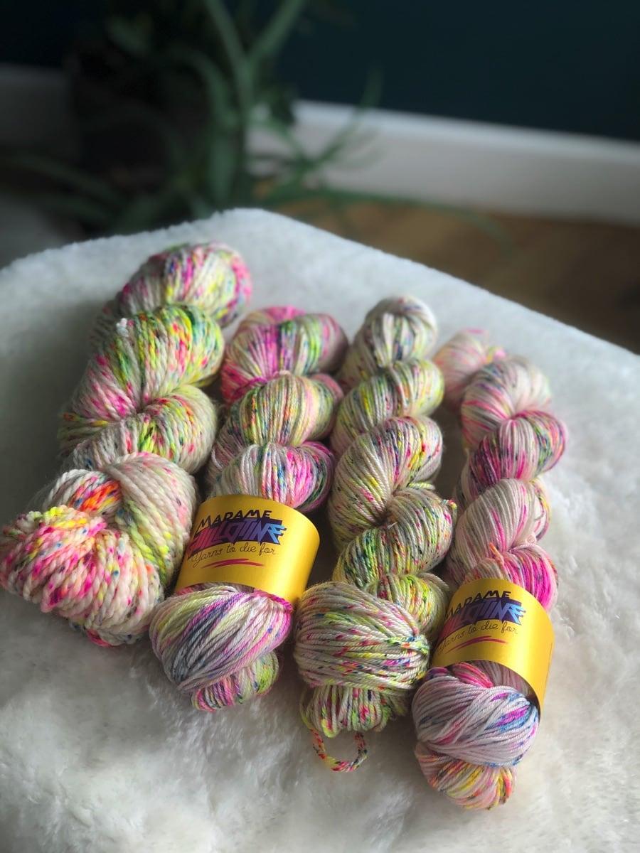 Quatre écheveaux de laine teinte à la main par Madame Guillotine avec des speckles fuchsia fluo, jaune fluo et bleu électrique