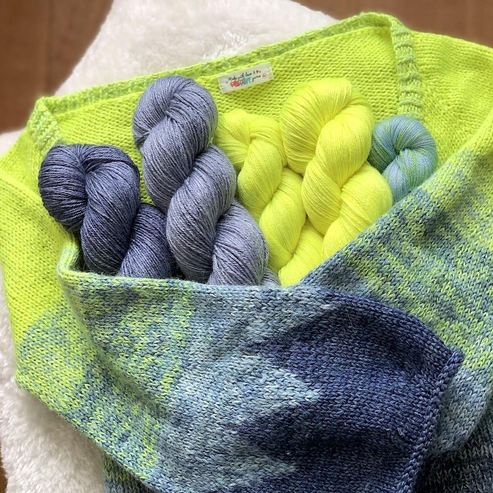 Un cardigan sur lequel sont posés des écheveaux de laine teinte à la main par Madame Guillotine