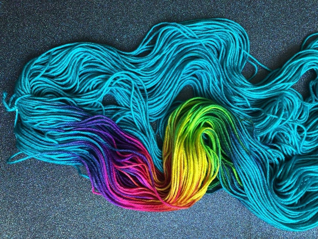 Un écheveau bleu turquoise teint à la main par Madame Guillotine étalé sur un fond pailleté