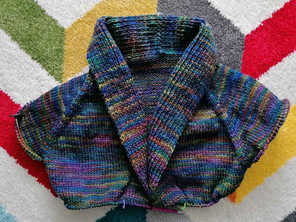 Un cardigan en train d'être tricoté main avec de la laine teinte à la main par Madame Guillotine dans le coloris Goth Rainbow
