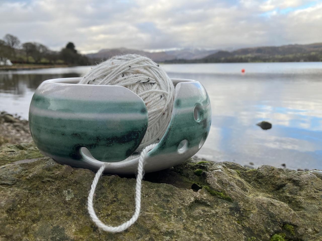White yarn bowl with a green band, in front of Ullswater. 