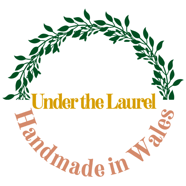 A round logo with a laurel wreath that states “Under the Laurel. Handmade in Wales”