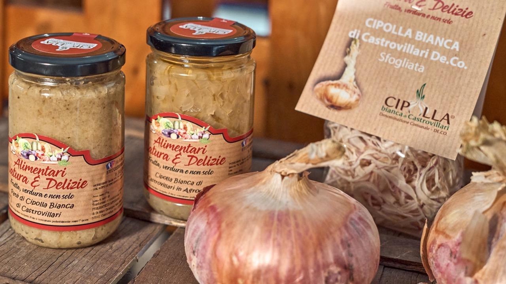 Vasetti “Natura & Delizie” con paté e cipolla bianca di Castrovillari De.Co., affiancati da cipolle fresche e confezione di cipolla sfogliata su sfondo rustico in legno.