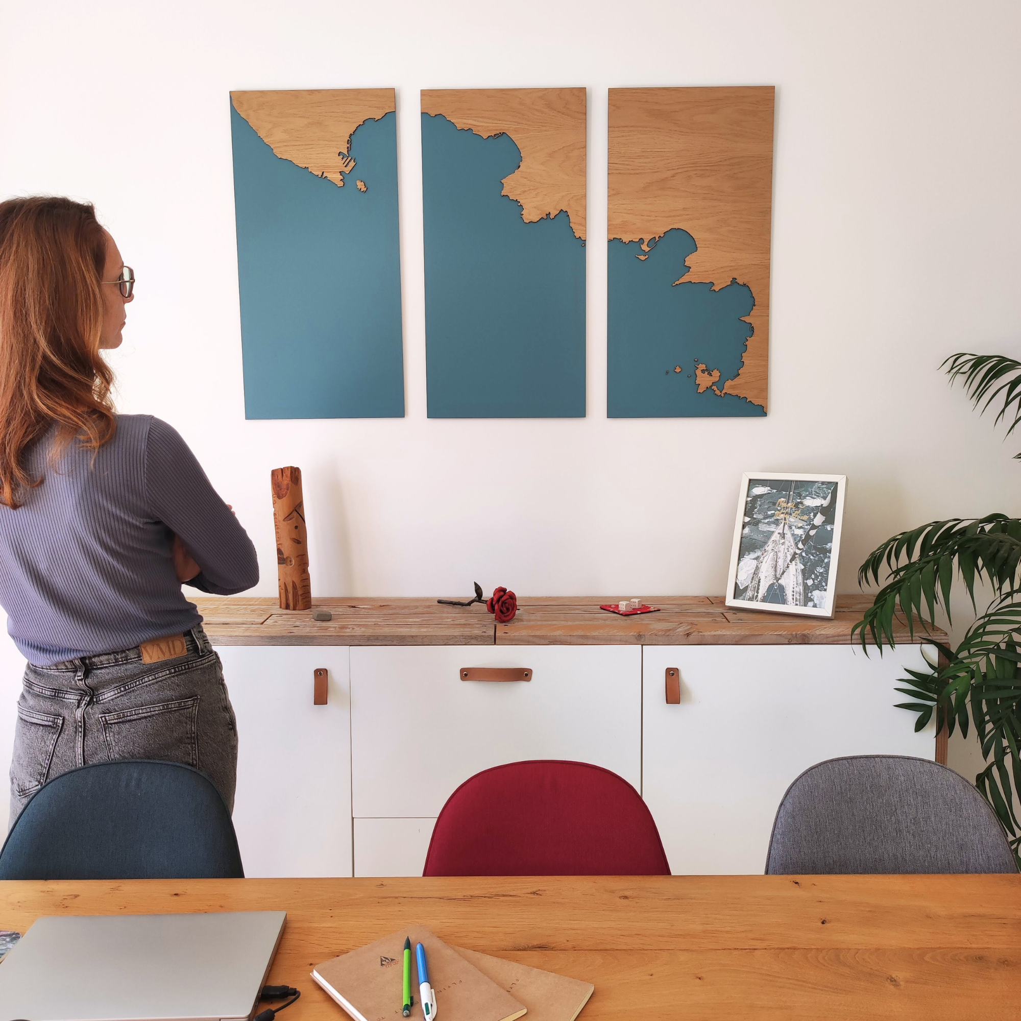 Marion, la créatrice de Litto-art observant un triptyque cartographique représentant le bord de mer dans une salle à manger tendance.