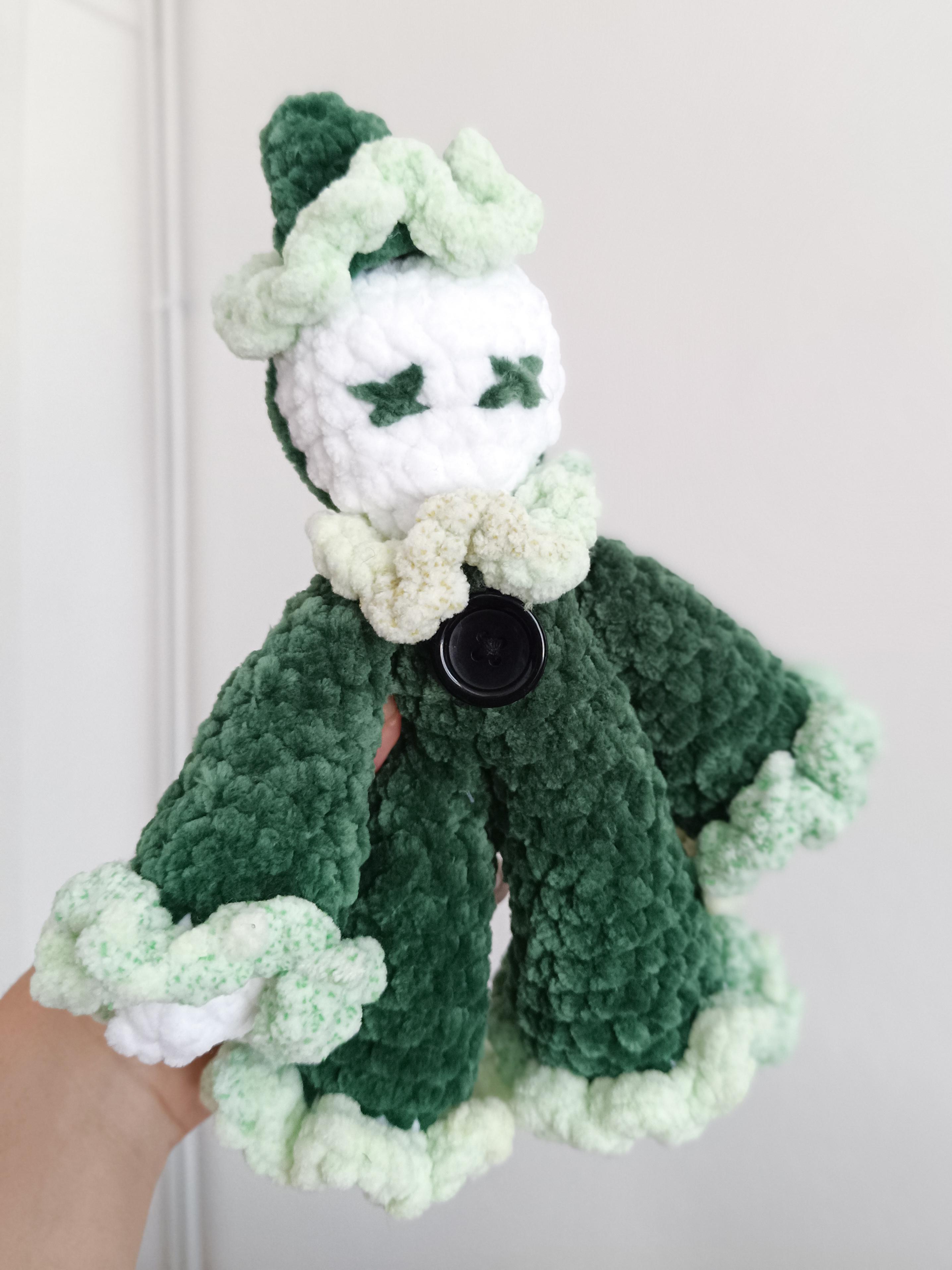 Un clown réalisé en crochet, en laine chenille, il est vert foncé vert clair au niveau des manches et de la collerette, sa tête est blanche.