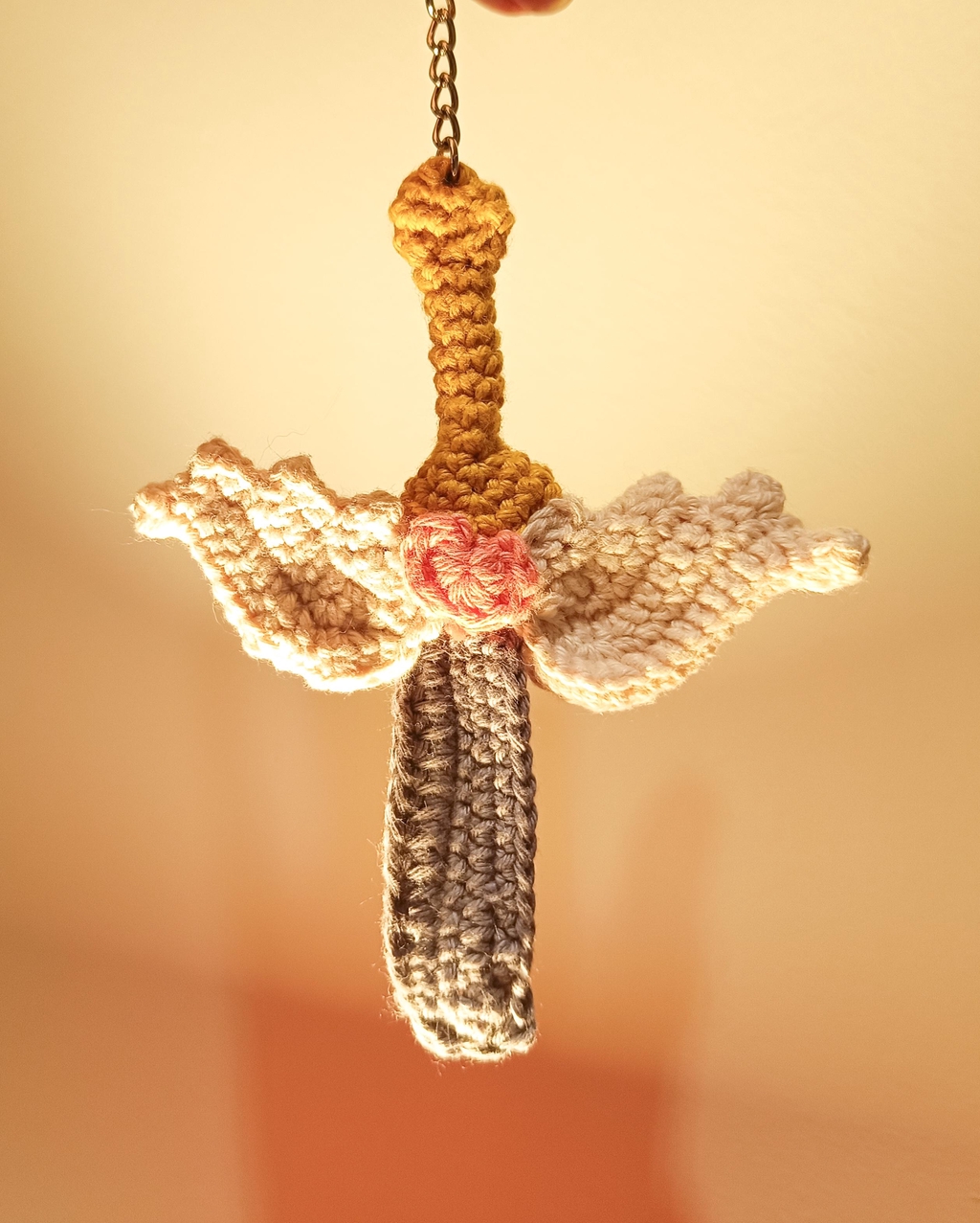 une petite épée avec des ailes ainsi qu'un cœur rose au milieu, en crochet.