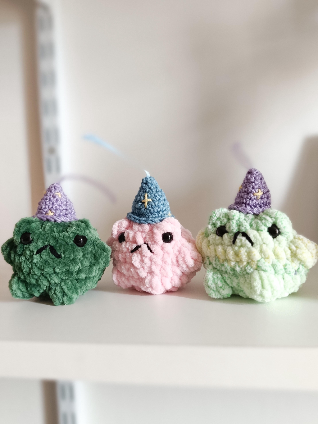 Trois petites grenouilles avec un chapeau pointu, une verte foncé, une rose et une verte claire.