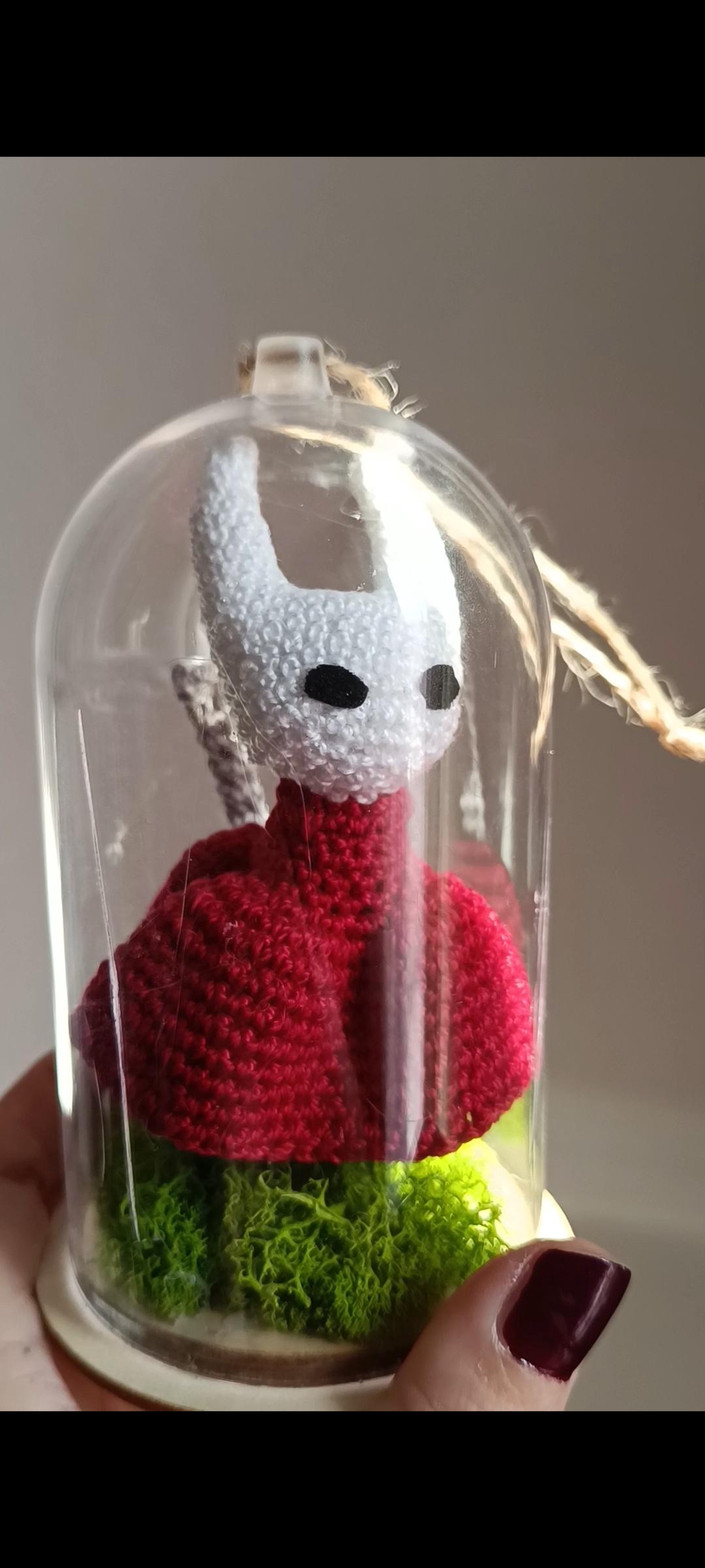 Une photo de Hornet de Hollow Knight, en crochet, sous une cloche en verre 