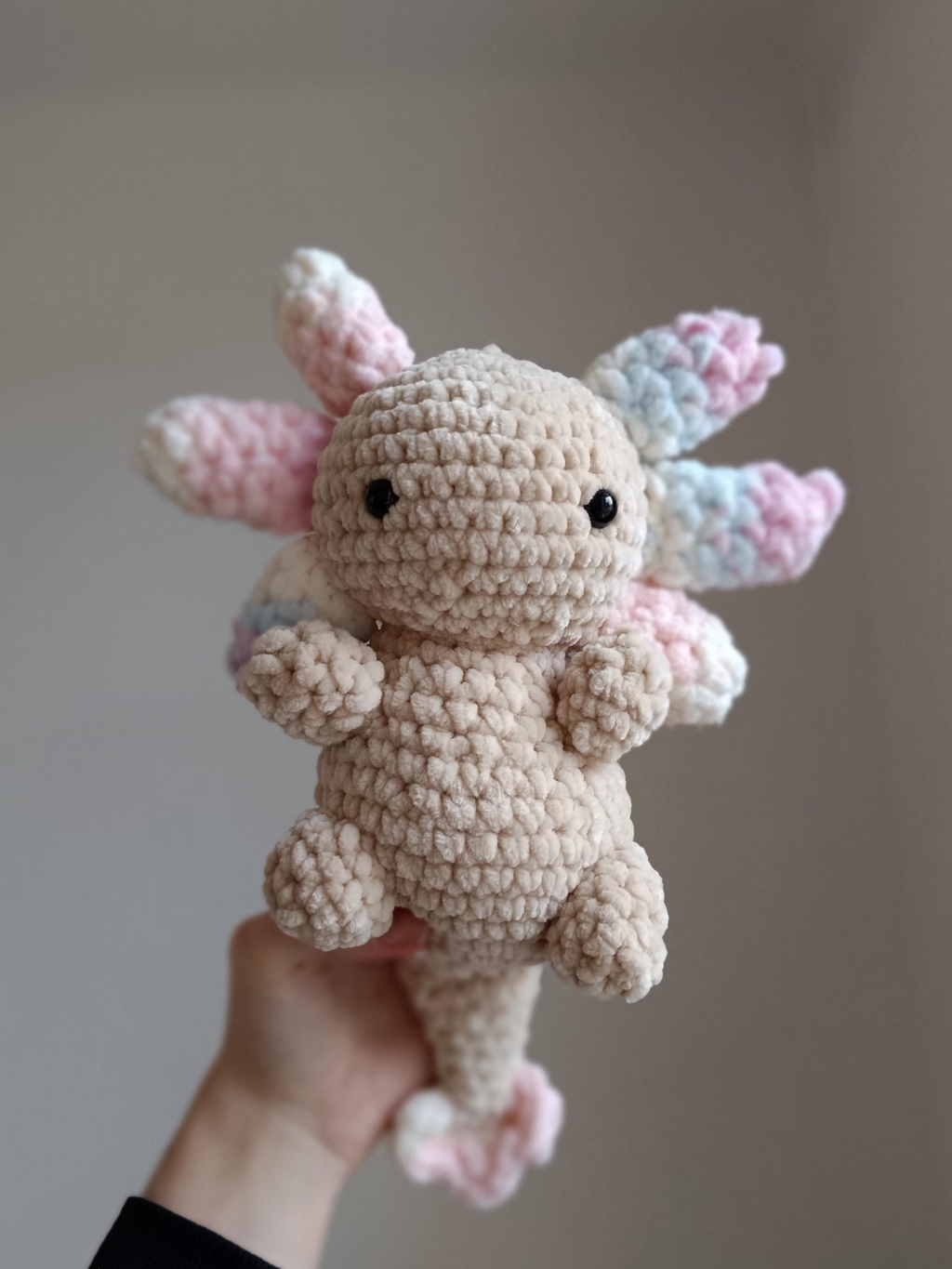 Un axolotl en crochet, beige avec les branchies multicolor pastels.