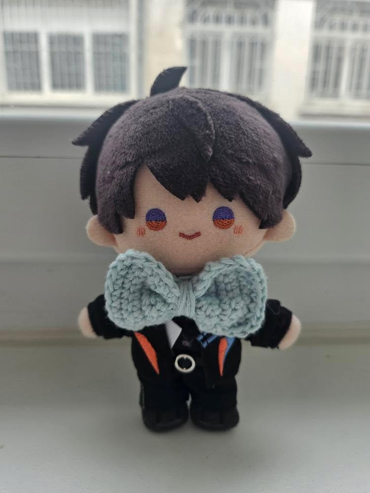 Une petite poupée, cheveux courts bruns, avec un petit noeud papillon bleu ciel réalisé au crochet.