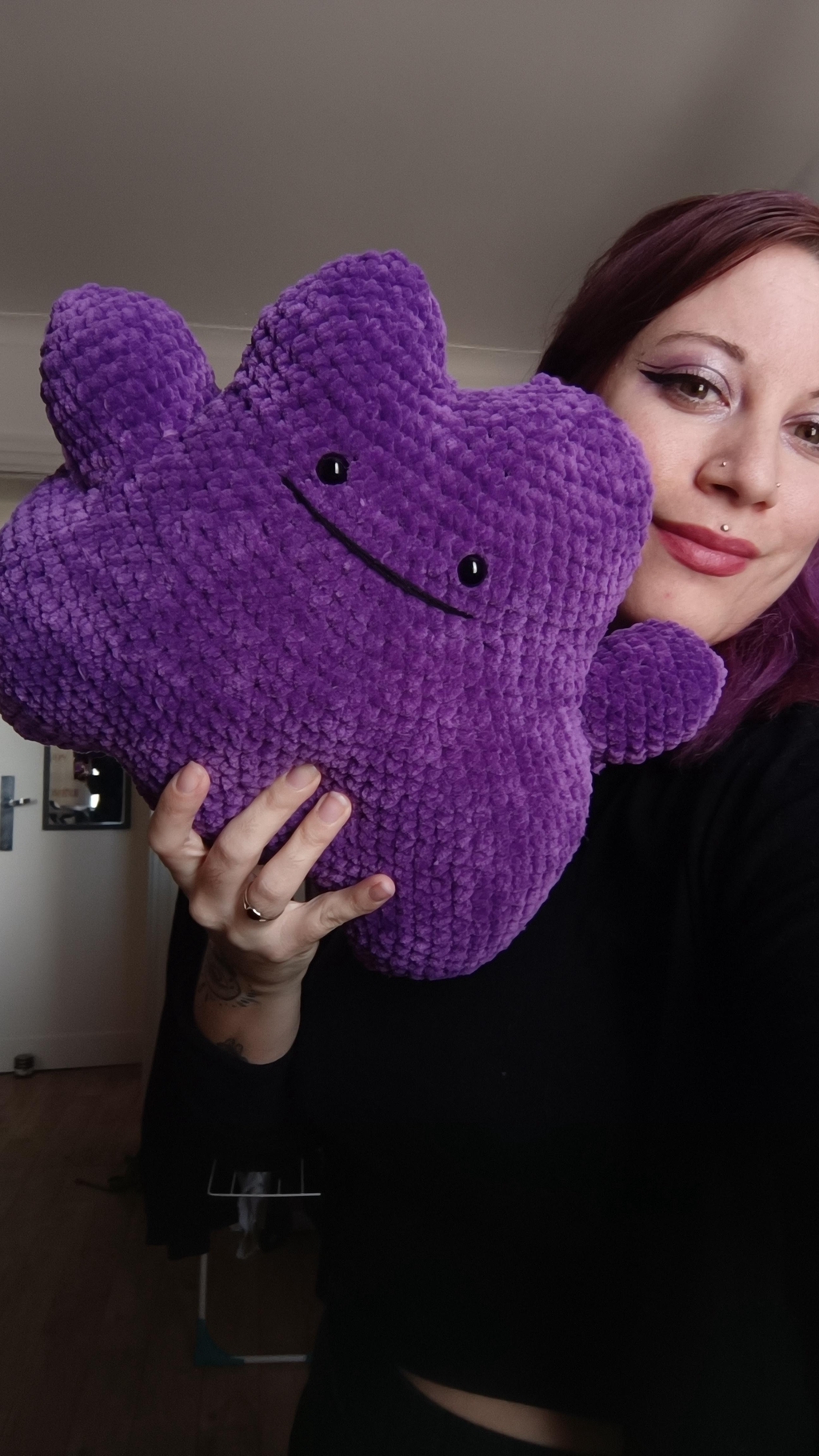 Un Pokémon Metamorph en peluche au crochet tenu dans une main de la créatrice, Violine, que l'on voit à droite de la photo, souriante.