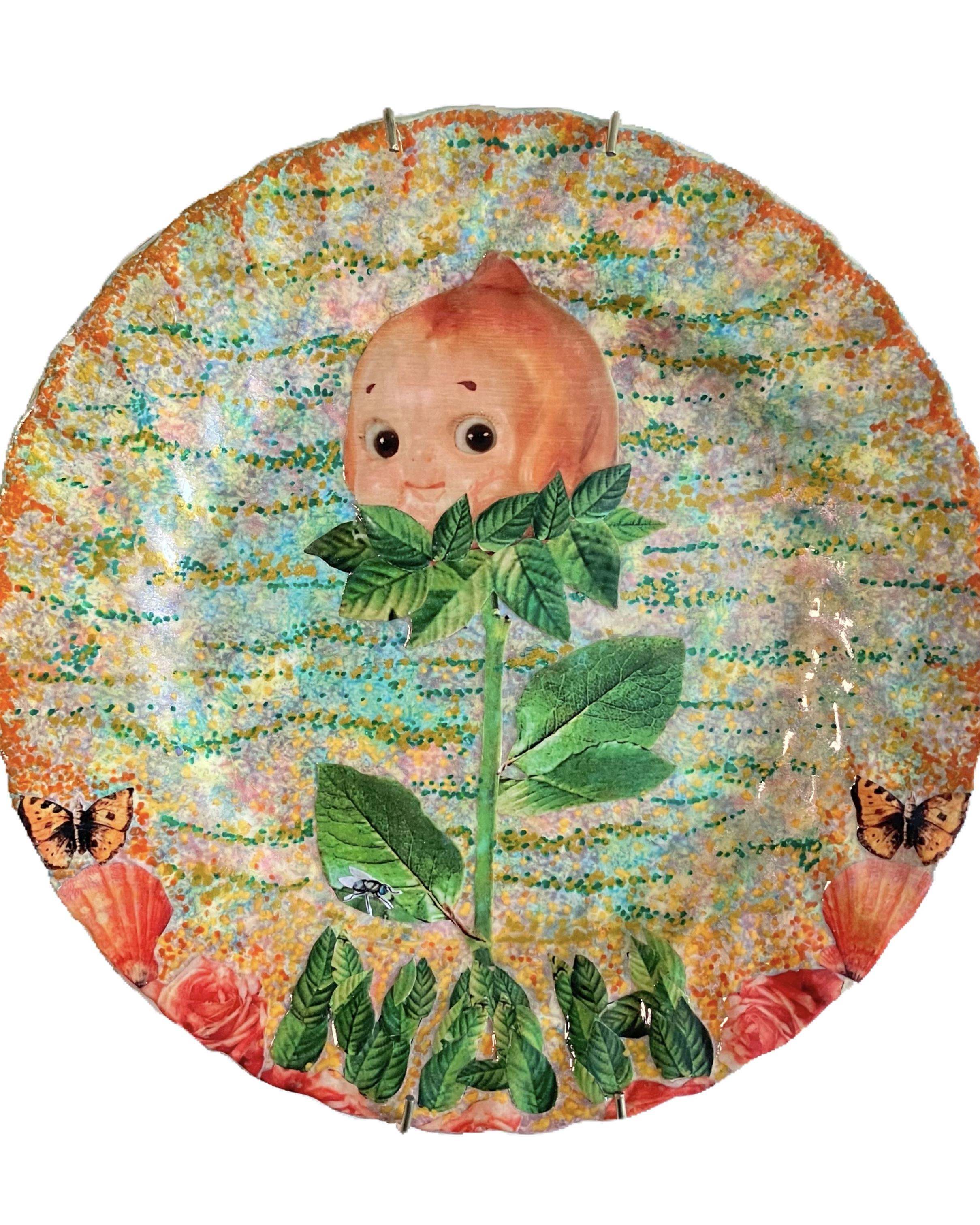 A vibrant collage artwork on a plate featuring a textured, colorful background in shades of orange, blue, and yellow. At the center is a large flower made from a doll's head, with green leaves and a stem, surrounded by smaller flowers and butterflies. At the bottom, the word 'NAH' is creatively spelled out using green leaves, adding a bold and playful touch to the piece.