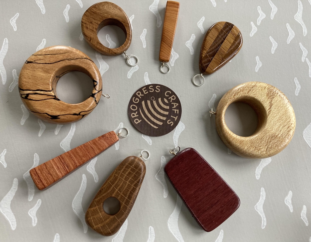 Progress Crafts heart logo with wooden pendants surrounding it made of different woods.