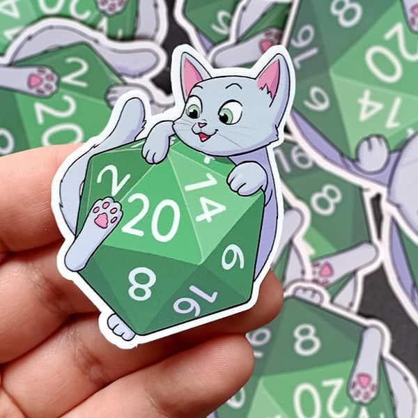 photo produit d'un sticker représentant un petit chat mignon et joyeux sur un D20 affichant un 20 de réussite critique
