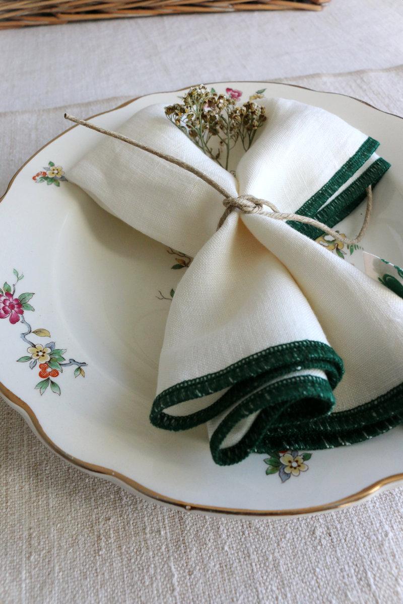 Assiette ancienne à décor floral avec serviette en lin ivoire, finition double surjet vert forêt, nouée d’une ficelle et ornée de fleurs séchées.