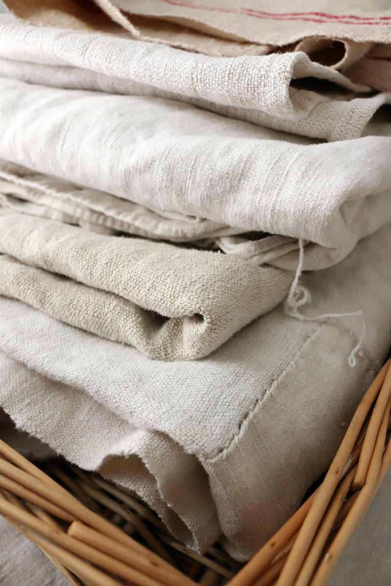 Textiles anciens en lin et chanvre pliés dans un panier en osier, présentés à côté du texte Ma manière de travailler.