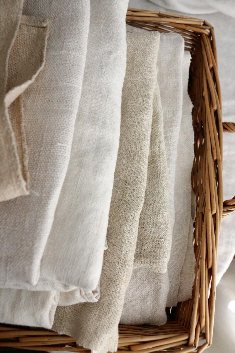 Textiles anciens en lin et chanvre, pliés dans un panier en fibres naturelles.