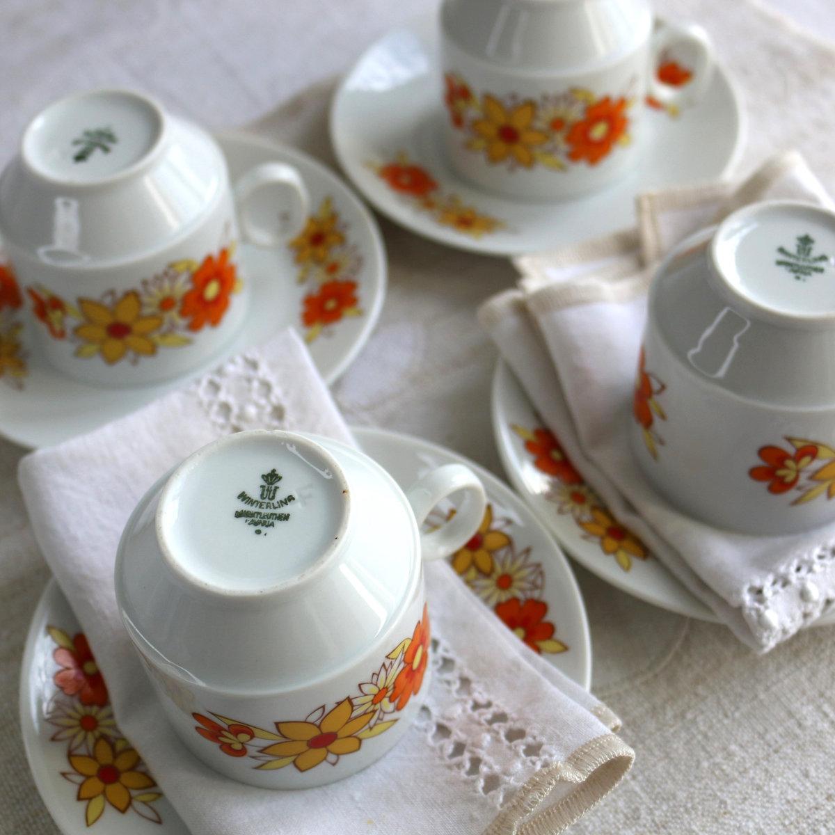 Tasses et soucoupes Winterling Marktleuthen décorées de motifs floraux orange et jaune, avec le tampon Winterling‑Marktleuthen‑Bavaria visible, posées sur serviette en lin blanc ancien ajouré.