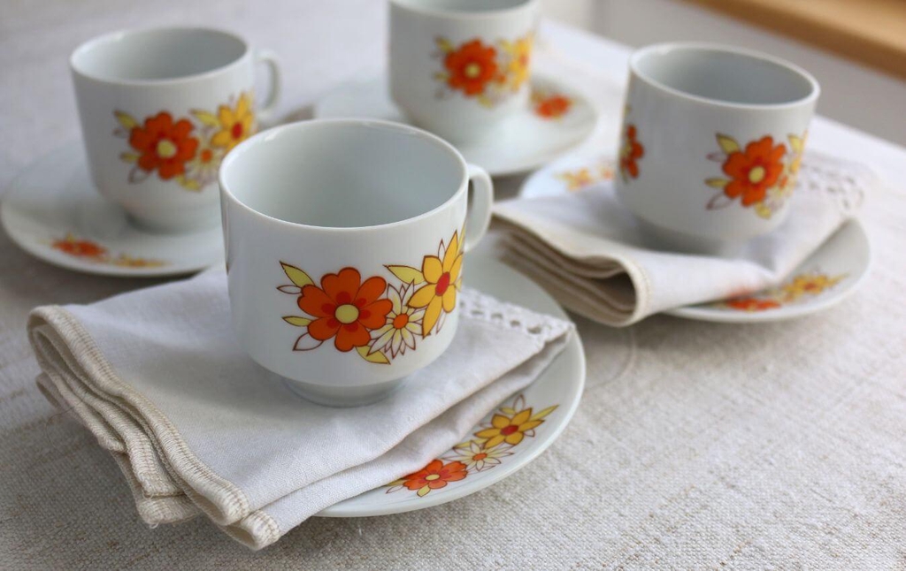 Tasses en porcelaine ancienne décorées de fleurs orange et jaunes, posées sur une serviette en lin ancien.