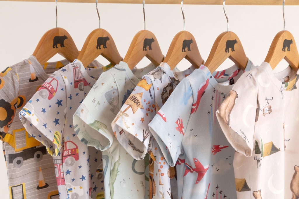 Six Lolabear t shirts are hung on wooden coathangers against a white background