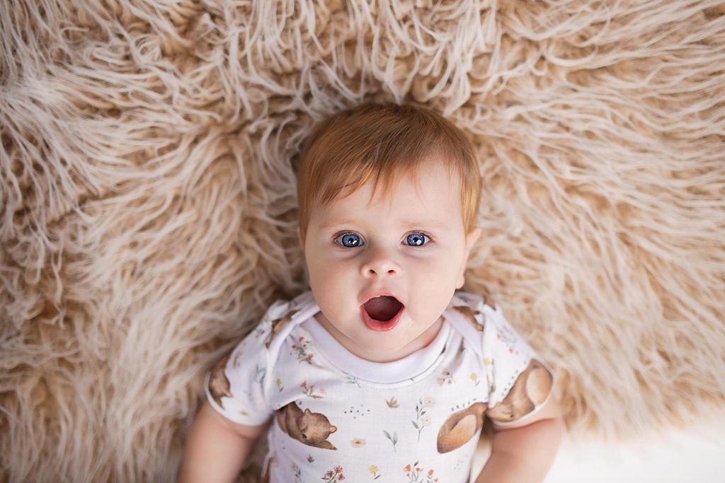 A baby looks up at the camera. She has big blue eyes and is wearing a Lolabear vest