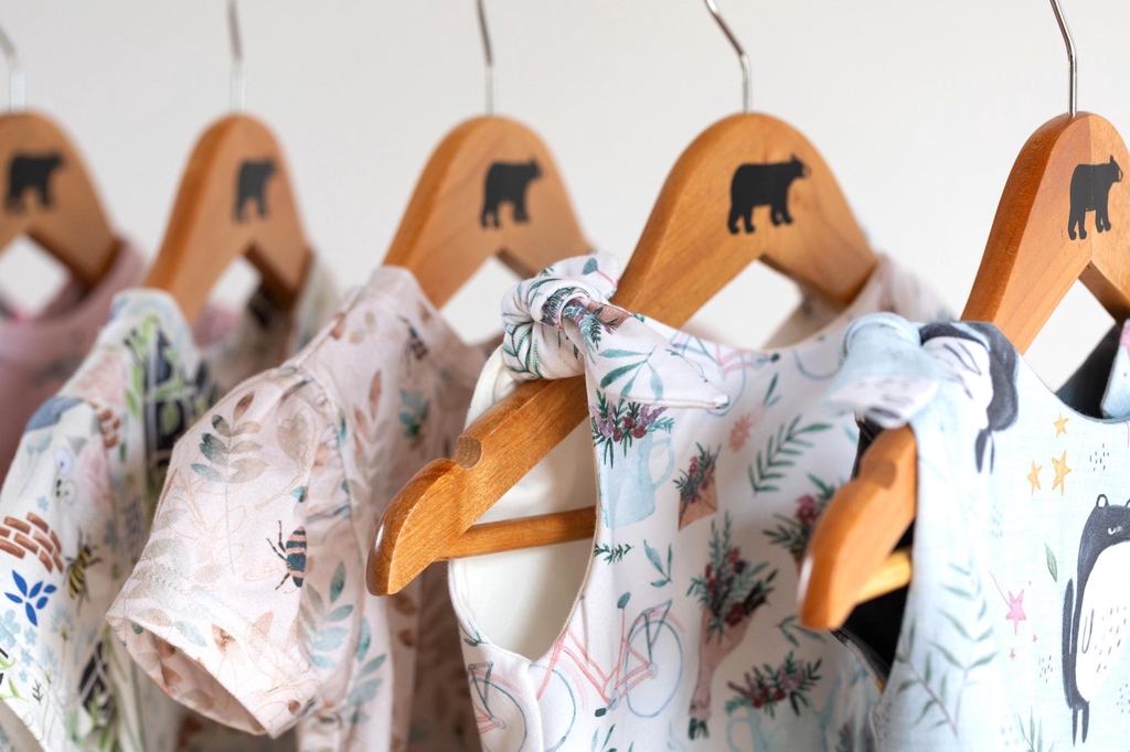 A row of Lolabear dresses hang on wooden coathangers. 