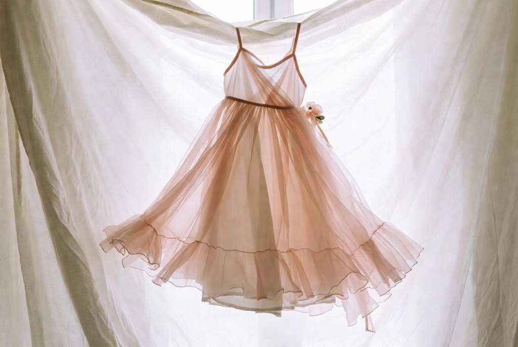 Jolie robe de demoiselle d’honneur ou tenue de cérémonie pour enfant en tissu fluide rose poudré et ivoire suspendue dans une lumière douce – Tenues enfants Maryline Devaux