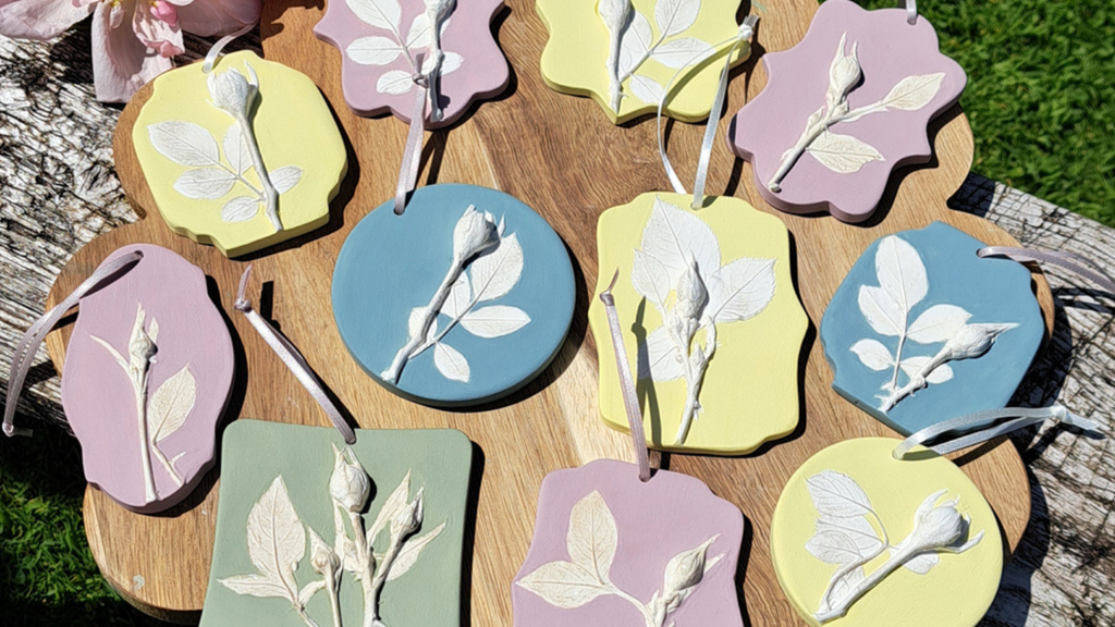 Image of small rose castings on a wooden board in a variety of shapes, painted in pastel greens, yellows, pinks and blues.