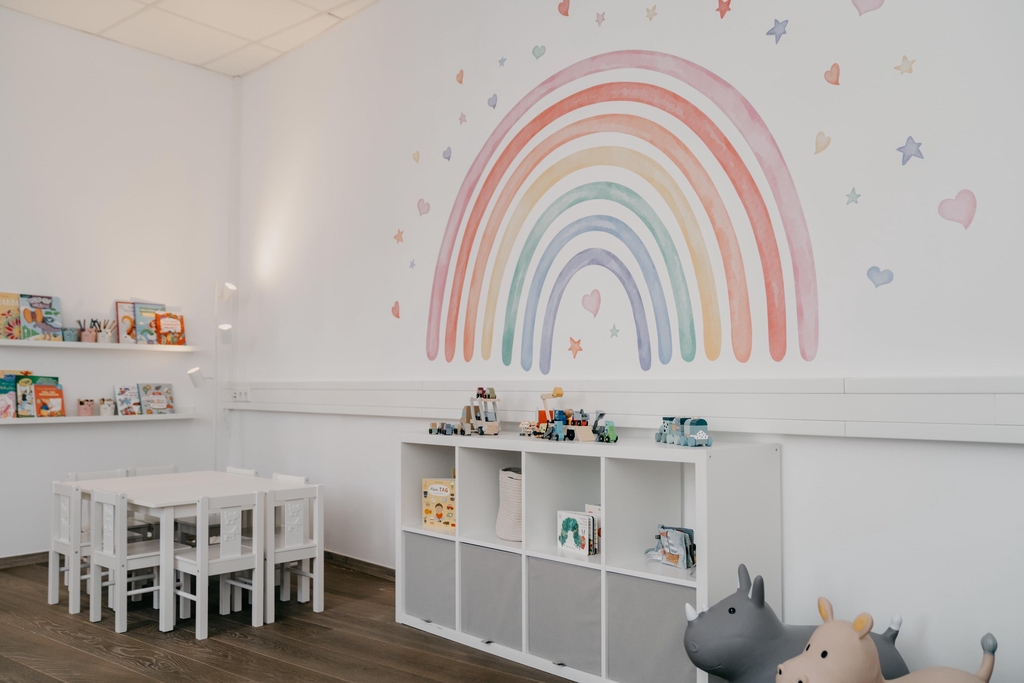 Ein Raum mit Spielsachen, Büchern und einem Regenbogen an der Wand