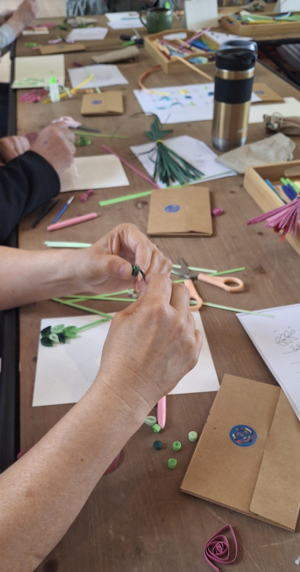 Quilling craft tools including paper strips, quilling tools, scissors, curling coach ruler, glue pots, paper, tweezers, all set out on a crafting table ready for a craft workshop.